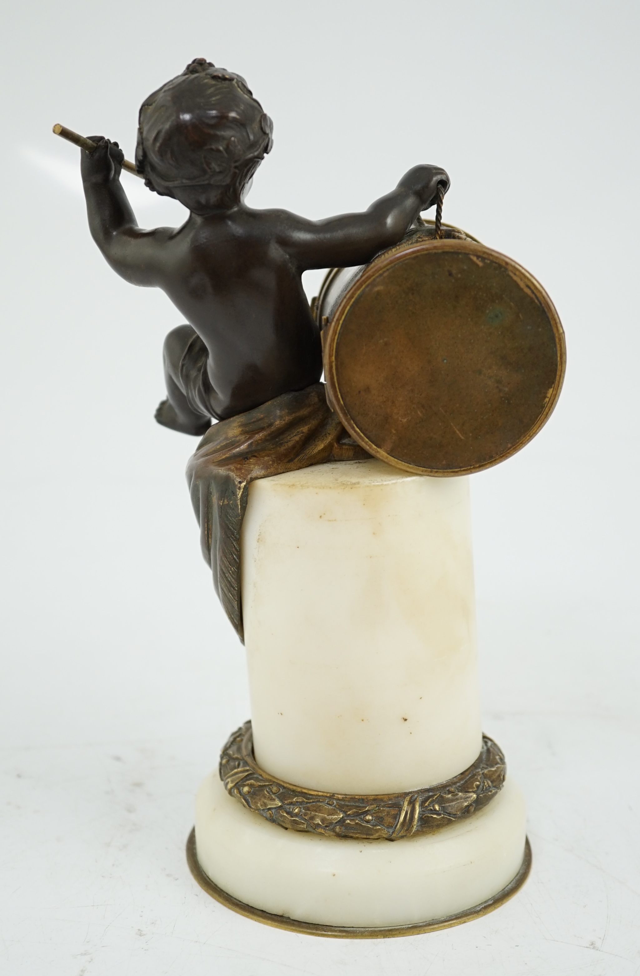 An early 20th century French eight day bronze and ormolu desk timepiece modelled as a putto banging upon a drum, with floral enamelled dial and white marble plinth, 12cm wide, 22.5cm high. Condition - good